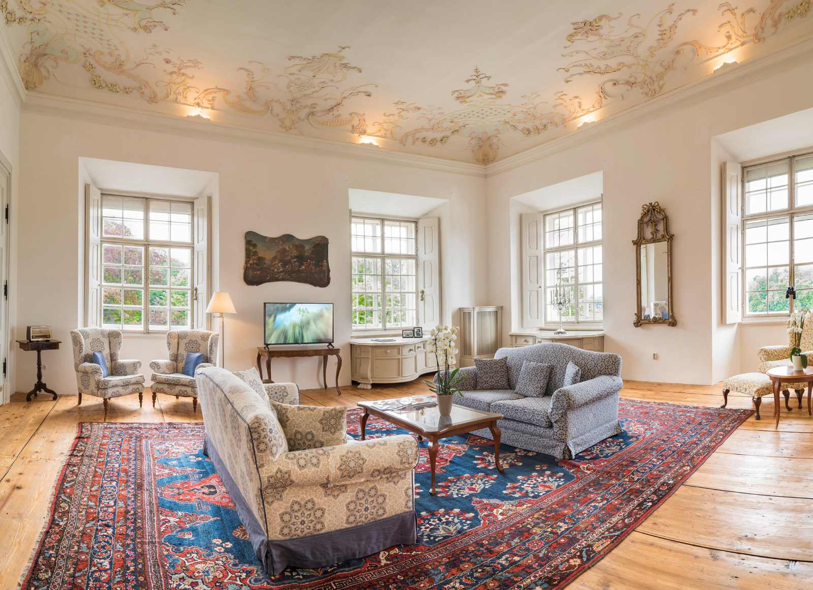 Eleganter Salon in Schloss Leopoldskron mit hohen Fenstern, Kronleuchter, Stuckdecke und klassischem Mobiliar.