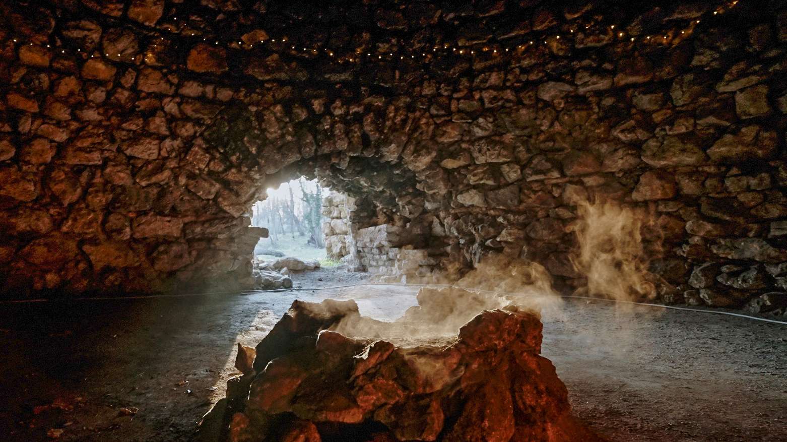 Steinerner Rundbau im Park von Schloss Schönau mit offener Toröffnung und dampfender Feuerstelle im Inneren.