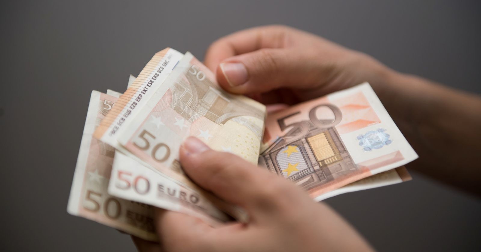 Sozialbetrug: Hände die mehrere 50-Euro-Banknoten halten.