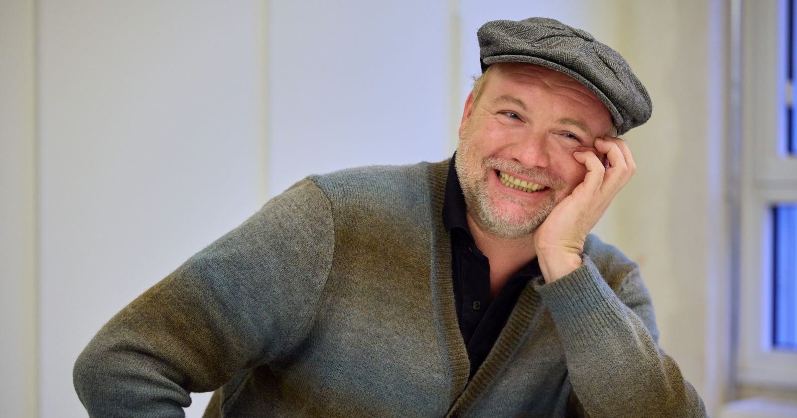 Thomas Stipsits mit grauer Kappe und Strickjacke lächelt/ Thomas Stipsits freut sich über tierischen Nachwuchs – süßer Hund erweitert seine Familie