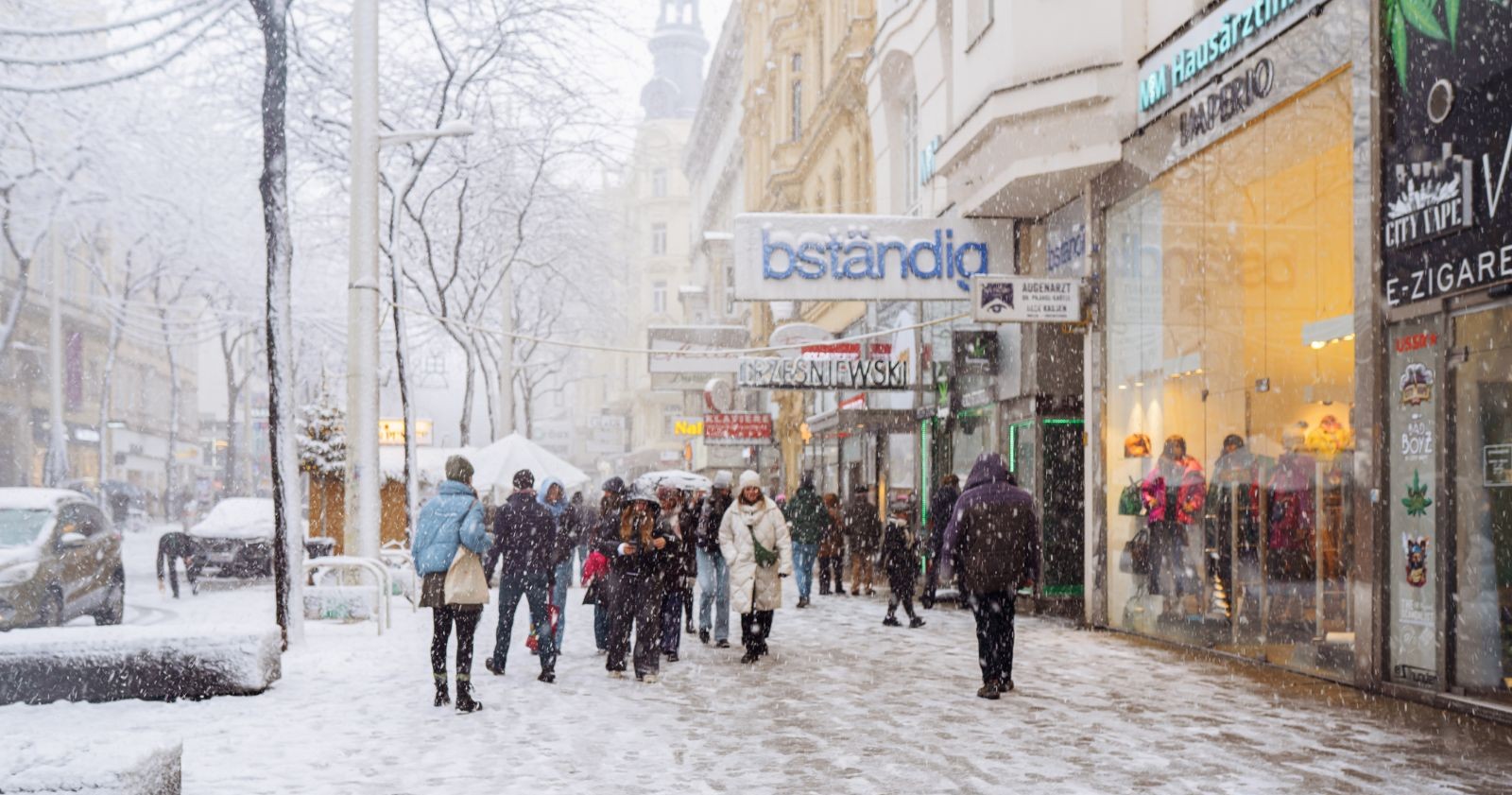 Wetter bringt Schnee in Wien: Menschen gehen durch eine verschneite Einkaufsstraße in Wien, dichter Schneefall und winterliche Stimmung in der Innenstadt.