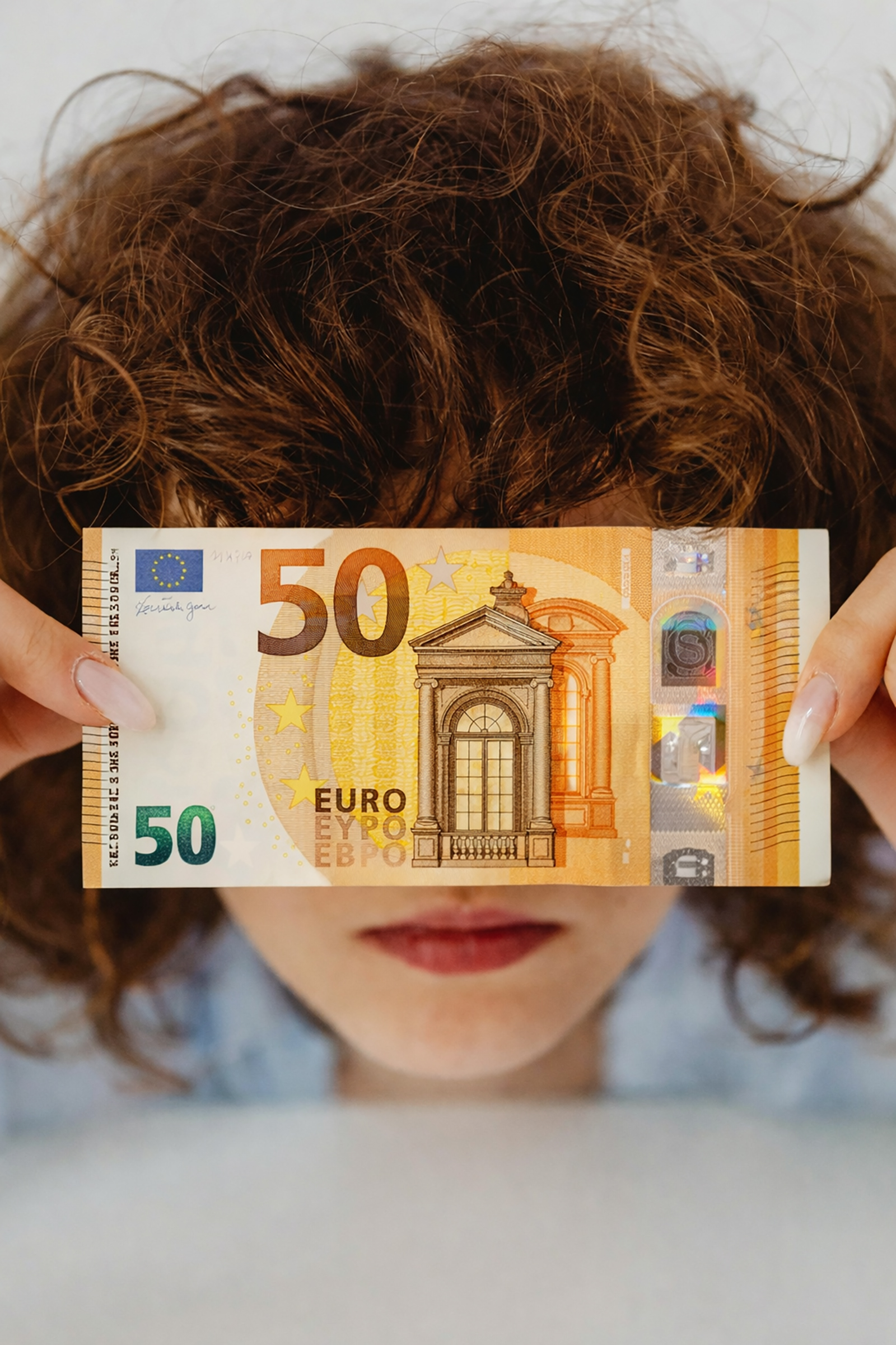 Junge Frau mit 50 Euro-Geldschein vor dem Gesicht | Credit: Trainingday