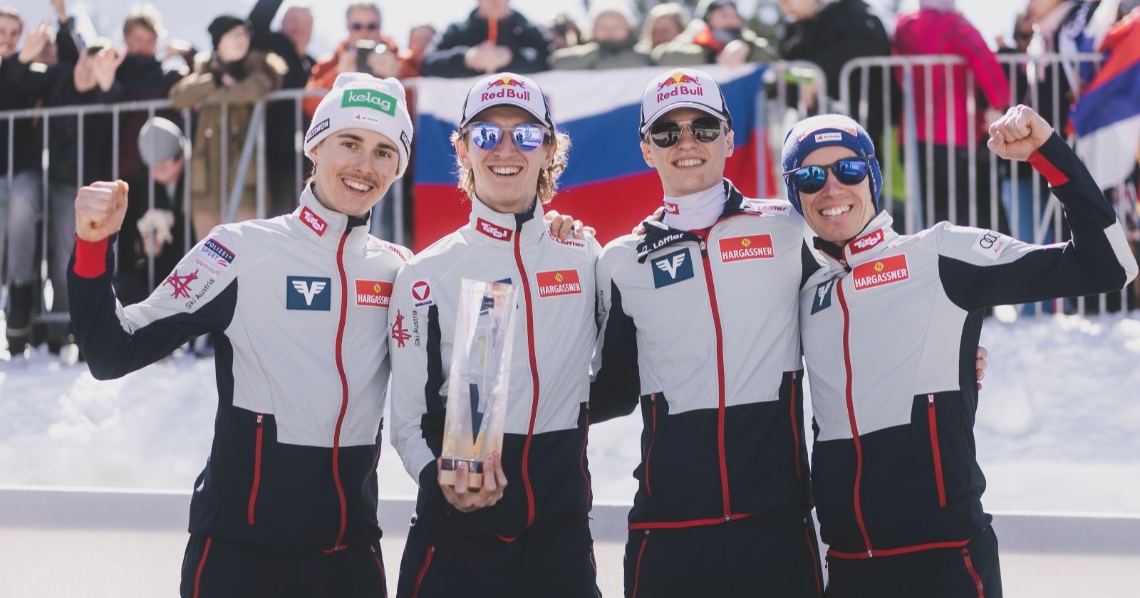 Vier Männer in Sportanzügen stehen vor Fans