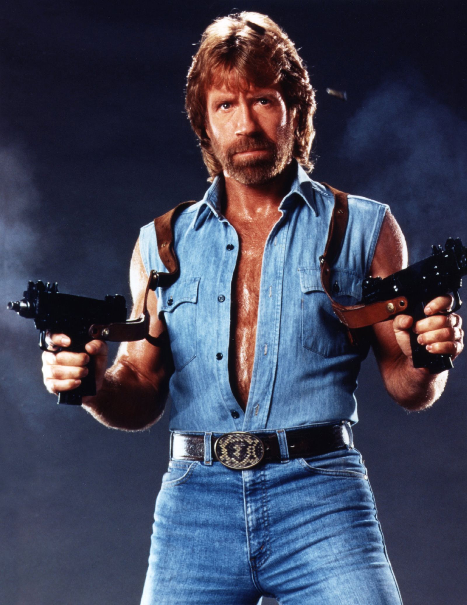 Chuck Norris posiert als Actionheld mit zwei Waffen und verkörpert die ikonische Stärke hinter den legendären Chuck Norris Witzen