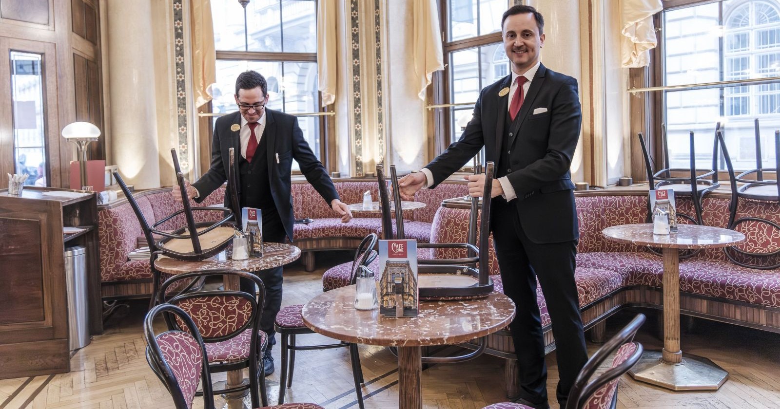 zwei Kellner stellen im Kaffeehaus die Sessel auf den Tisch