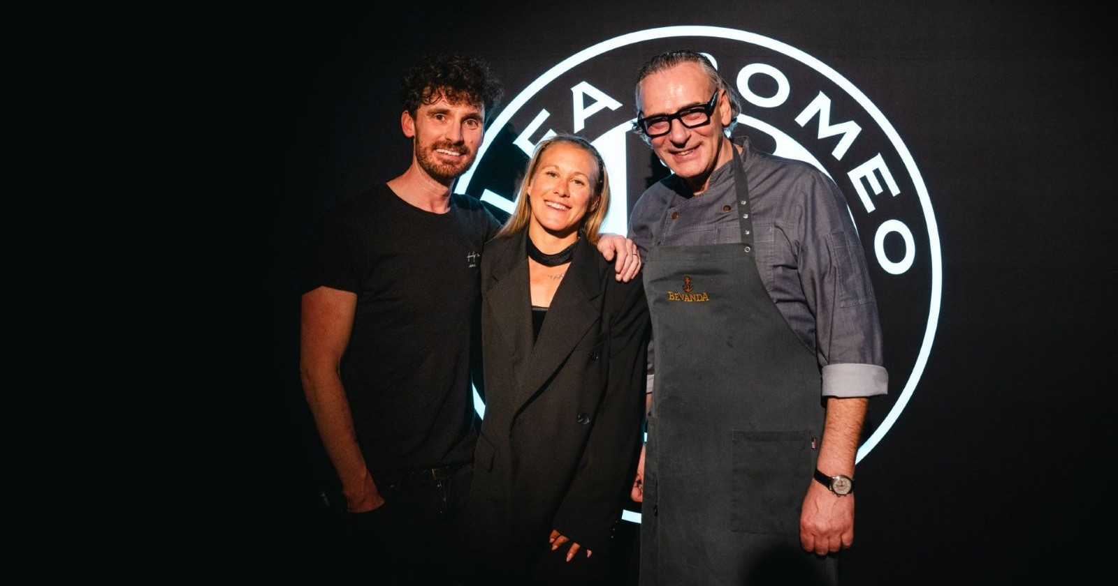 Trio in schwarzer Kleidung vor einem Auto-Logo