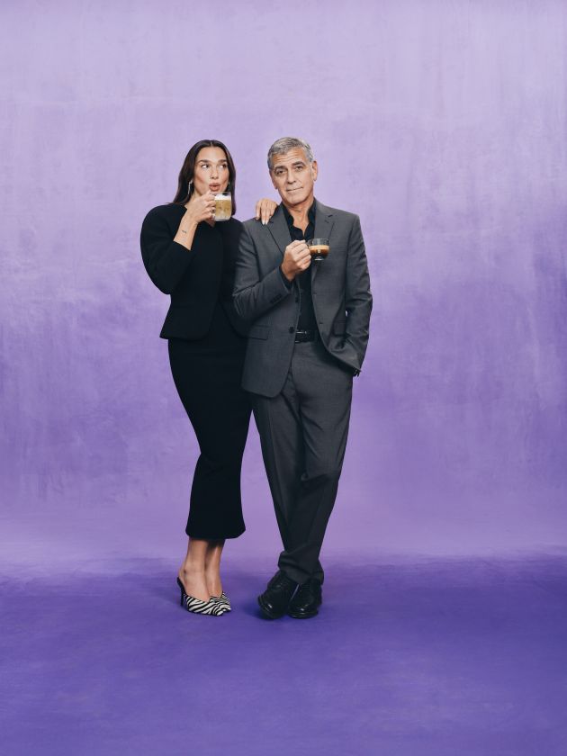 Kampagnenmotiv zu Dua Lipa und George Clooney für Nespresso: Frau und Mann in eleganter Kleidung trinken Kaffee vor violettem Hintergrund