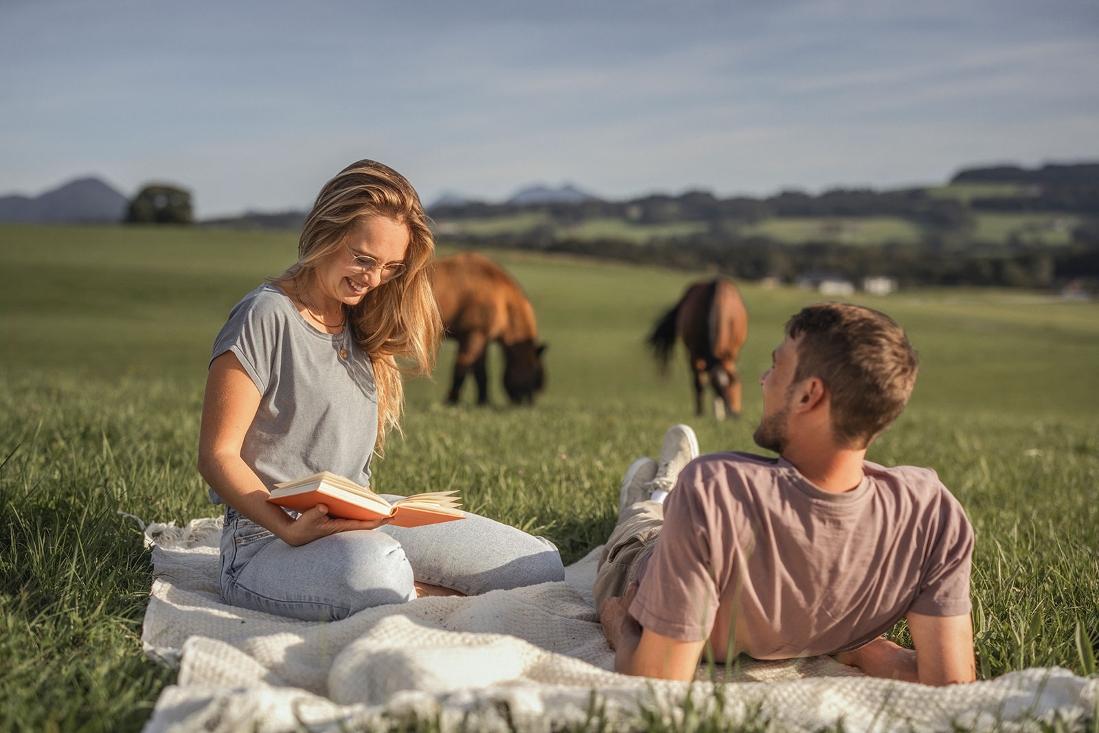 Mann und Frau sitzen in der Landschaft auf einer Decke im Hintergrund weiden Tiere | Credit: Michael Grössinger