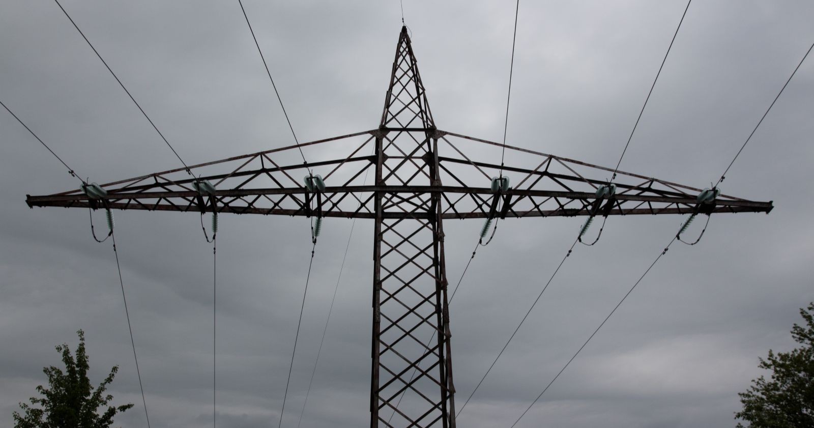 Ein Strommasten unter einem grauen, wolkenverhangenen Himmel.