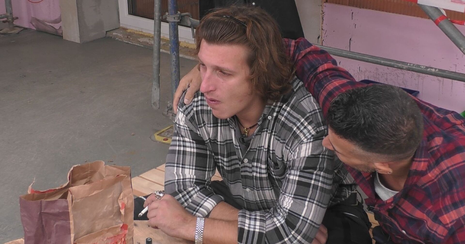 Satans Bratan sitzt am Boden neben einer Baustelle, hält eine Zigarette in der Hand/ Satans Bratan hatte einen Unfall und zeigt sich im Rollstuhl,