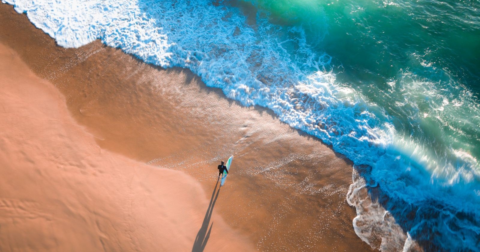 Ein Surfer geht vom Strand in das Meer.
