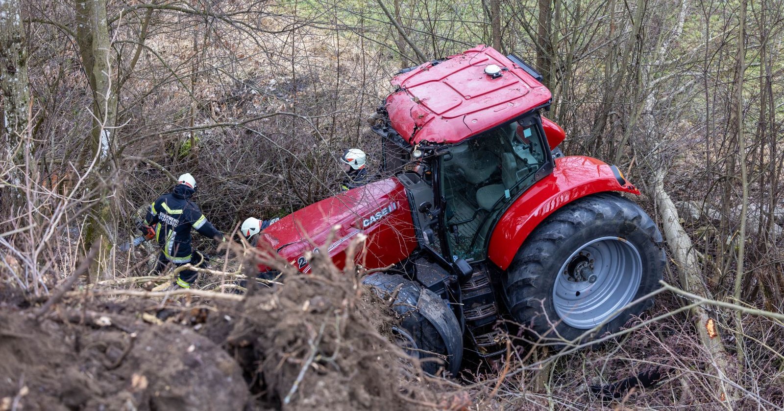 Ein roter Traktor hängt im Gebüsch, rundherum sind Feuerwehrleute