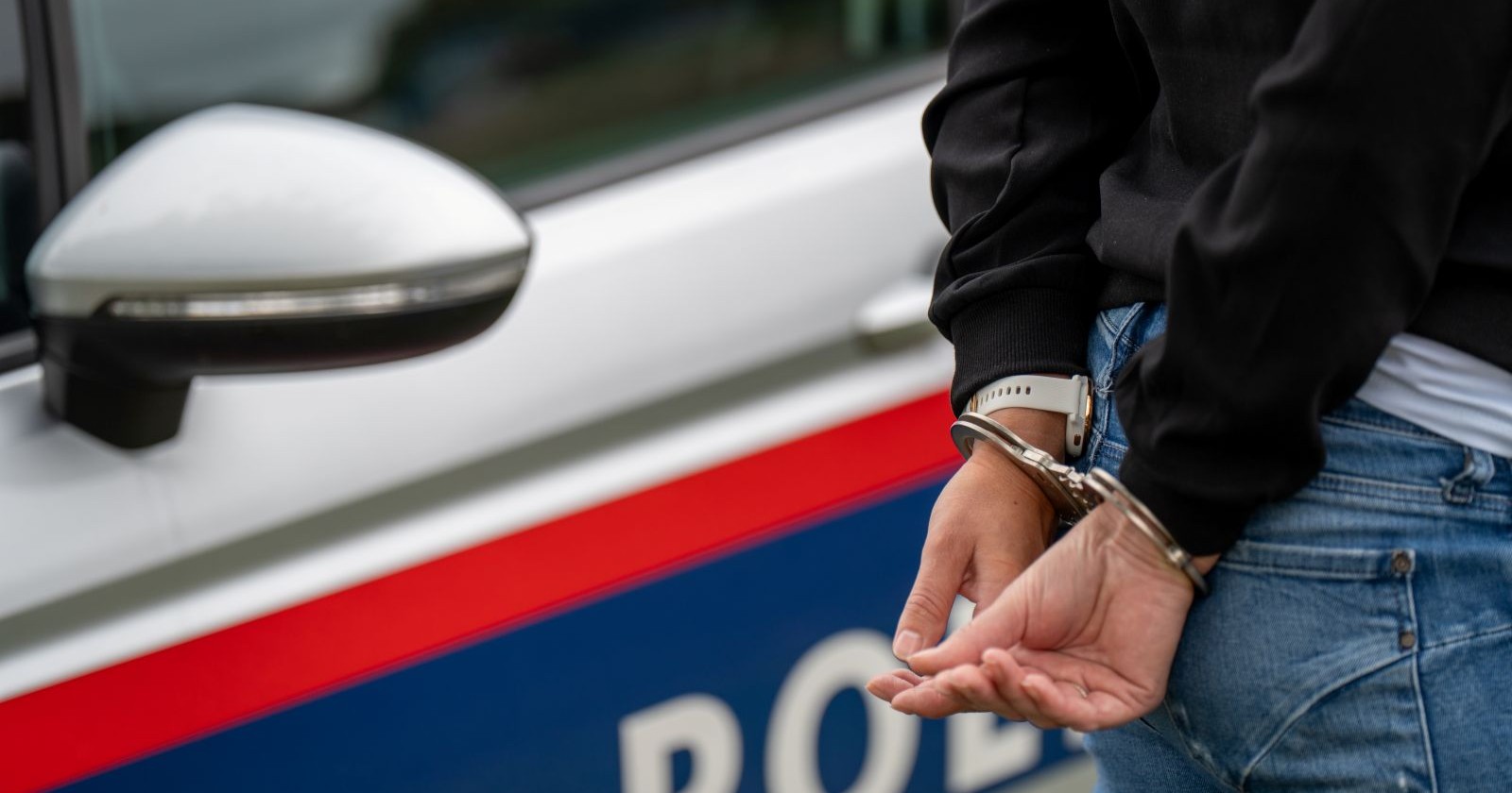 Mann in Handschellen, dahinter steht ein Polizeiauto