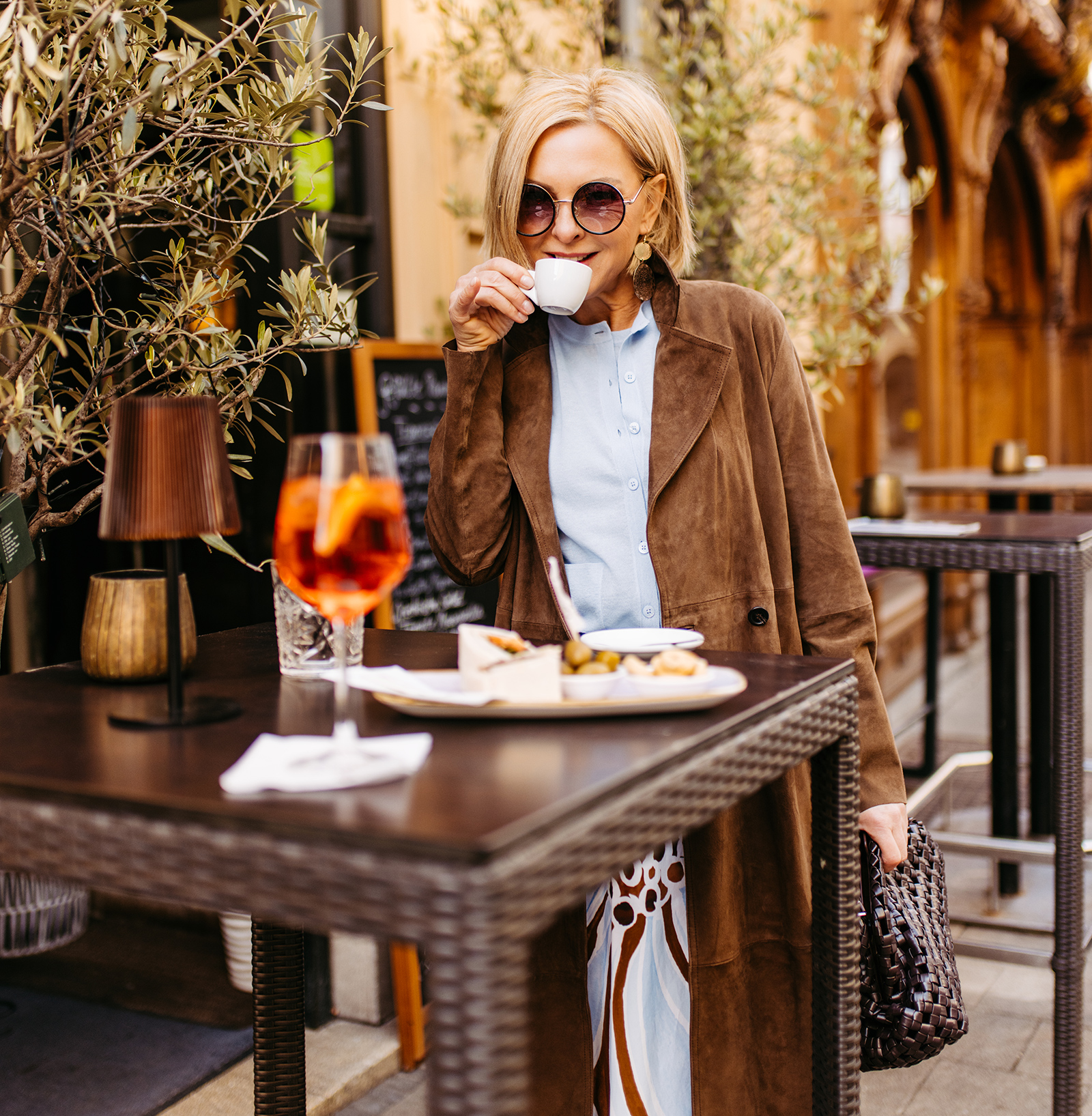 Elegant gekleidete Frau trinkt aus der Tasse in einem Straßencafé | Credit: Benjamin Gasser