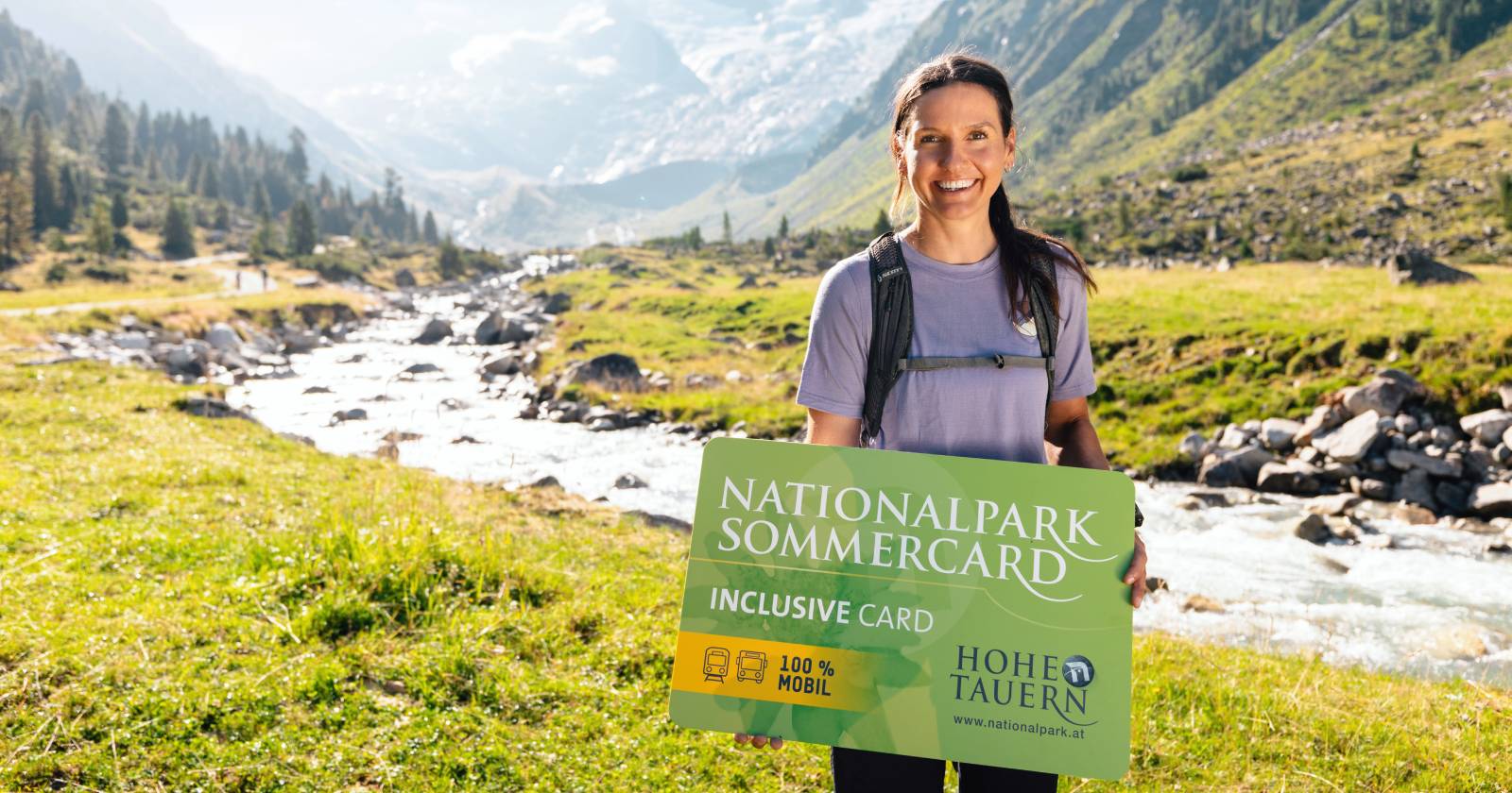 Frau mit Rucksack bei Wanderung mit dem Nationalpark Sommercard Banner in der Hand | Credit: Ferienregion Nationalpark Hohe Tauern/Mathäus Gartner