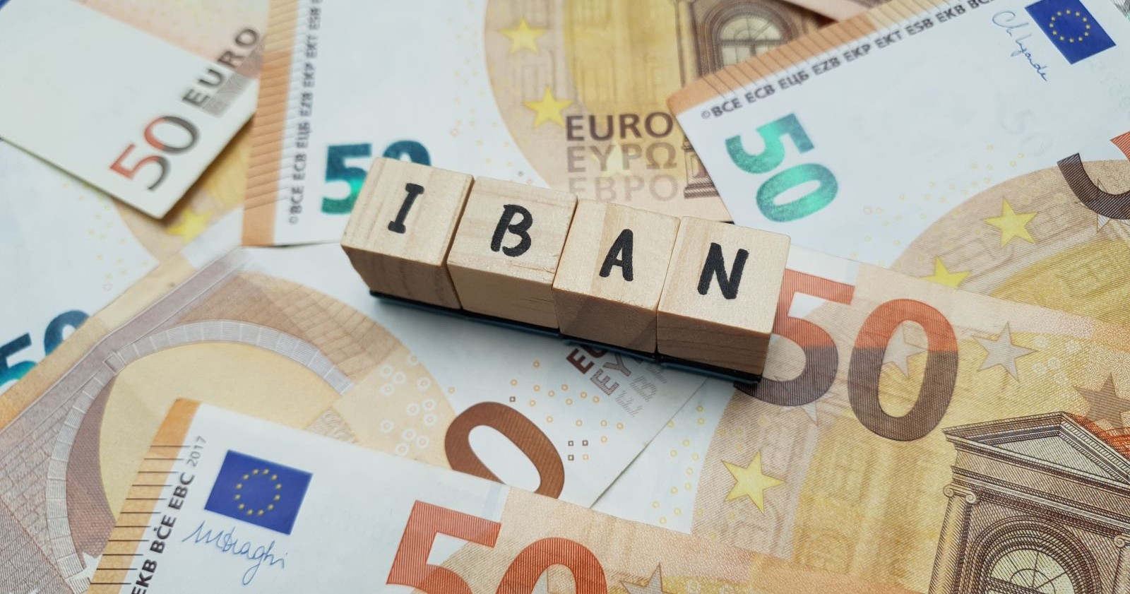 50 Euro-Banknoten hinter Holzklötzen auf denen das Wort "IBAN" geschrieben steht