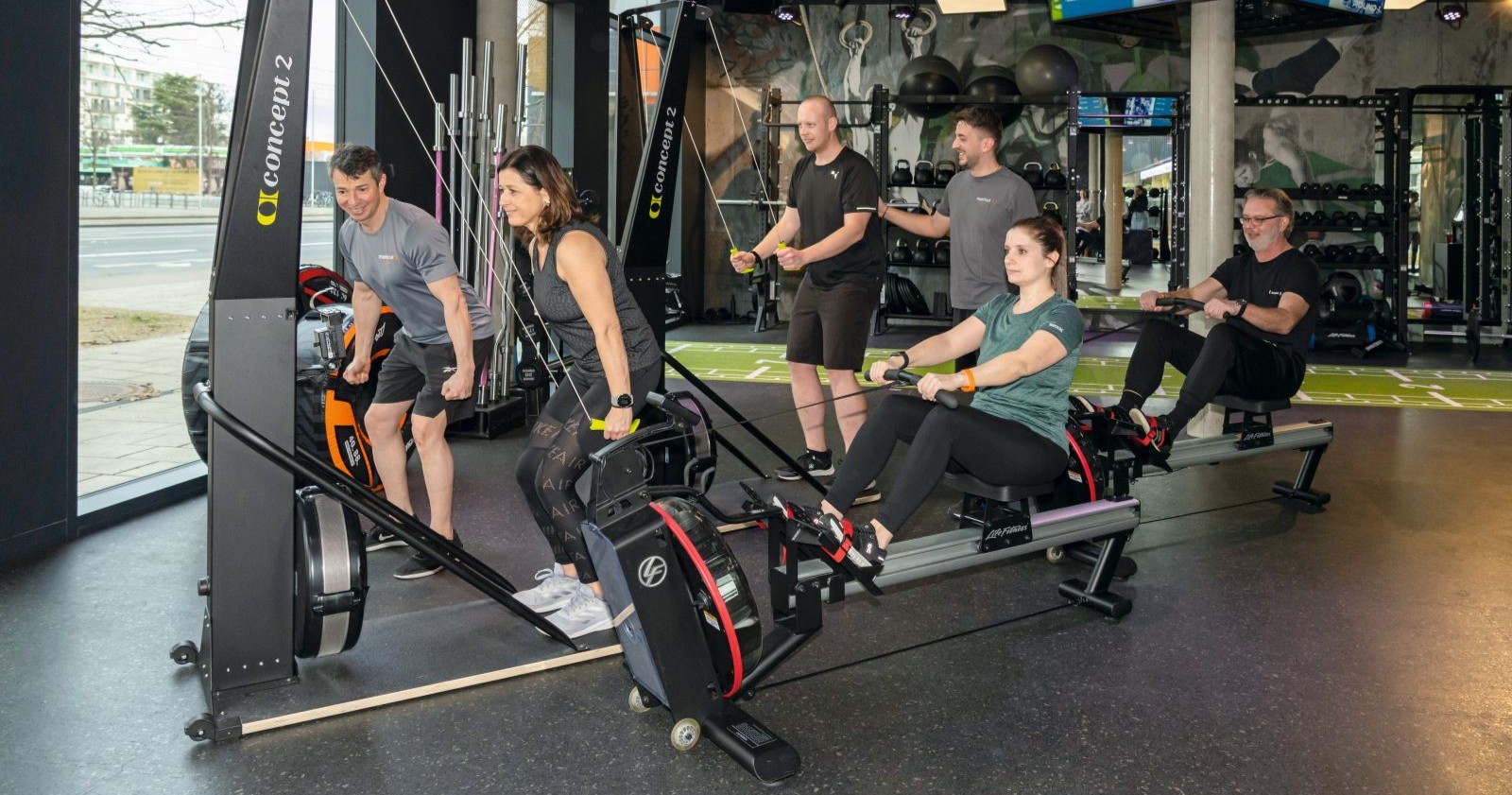 Mehrere Menschen trainieren auf einem Rudergerät
