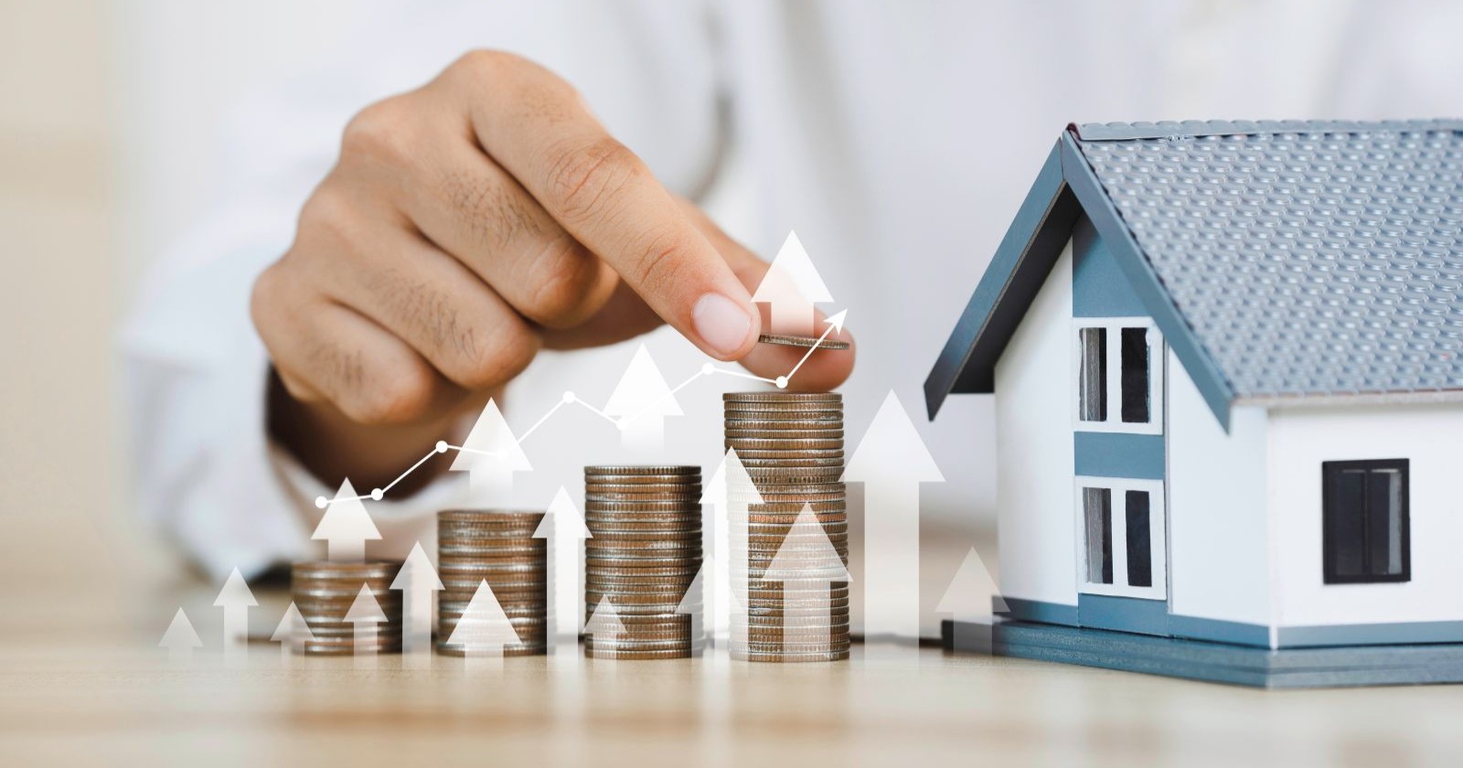 Modell eines Hauses, eine Männerhand legt Münzen auf einen Stapel