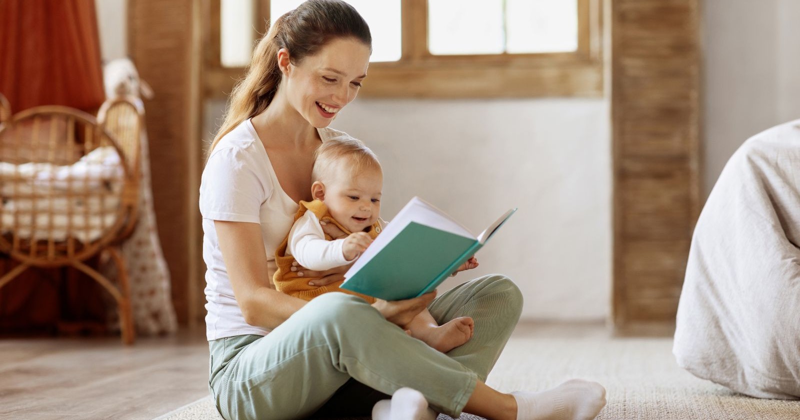 Frau sitzt am Boden und liest Baby vor