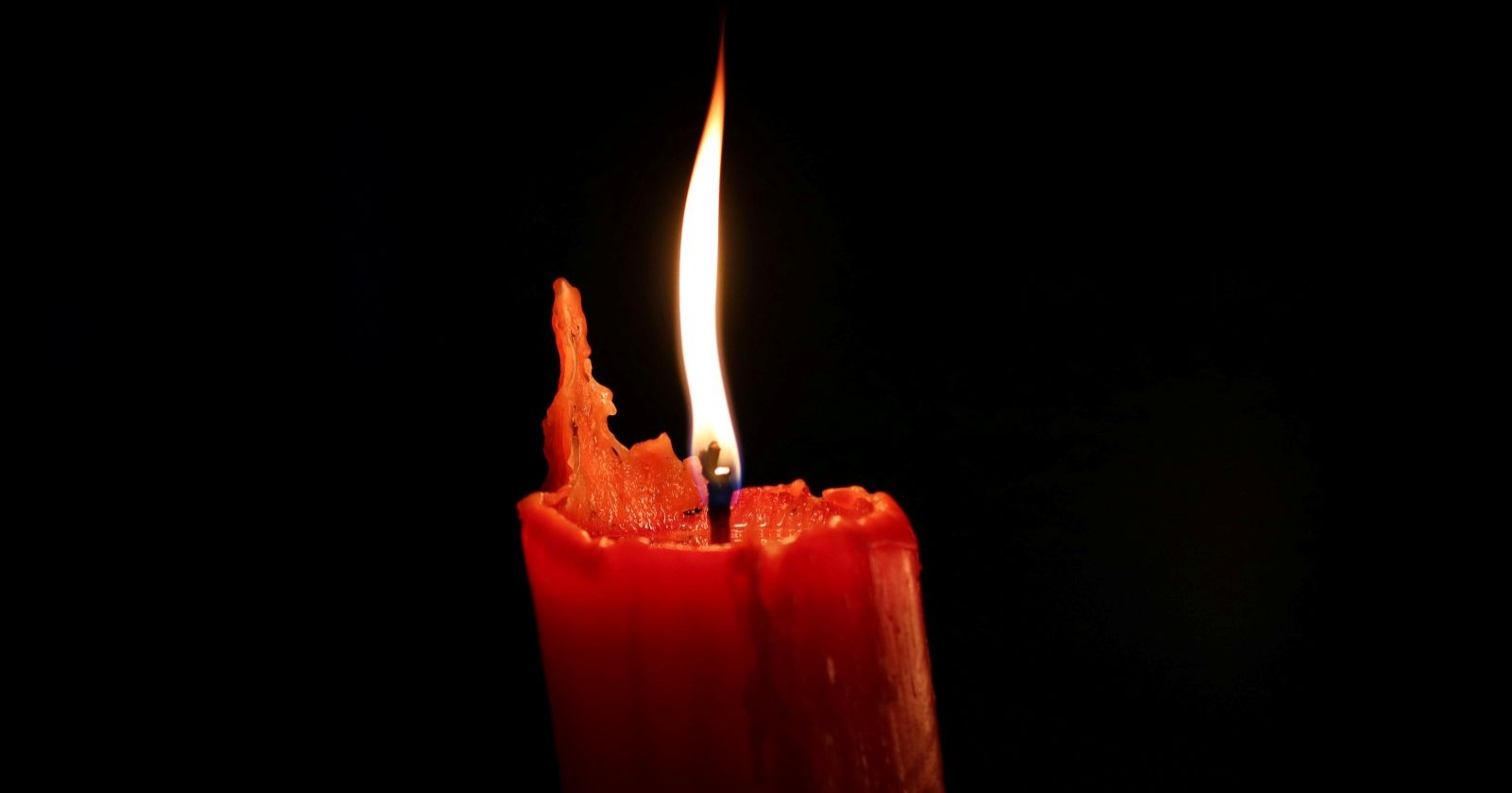 Rote Kerze mit Flamme im Dunkeln als Symbol für Trauer um das Baby, das durch einen Querschläger getötet worden ist.