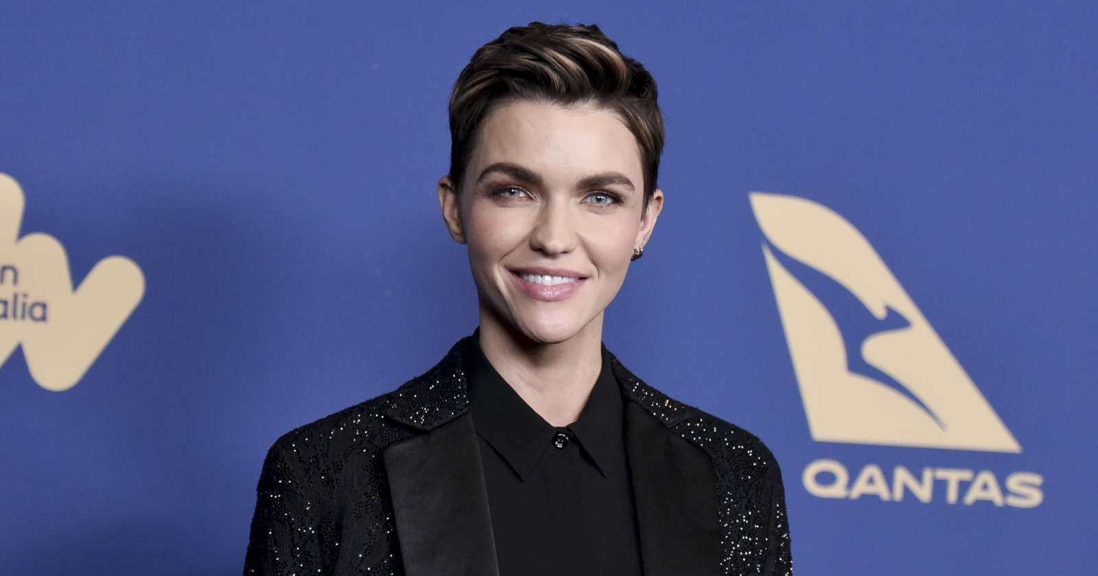 Ruby Rose lächelnd vor einer blauen Wand