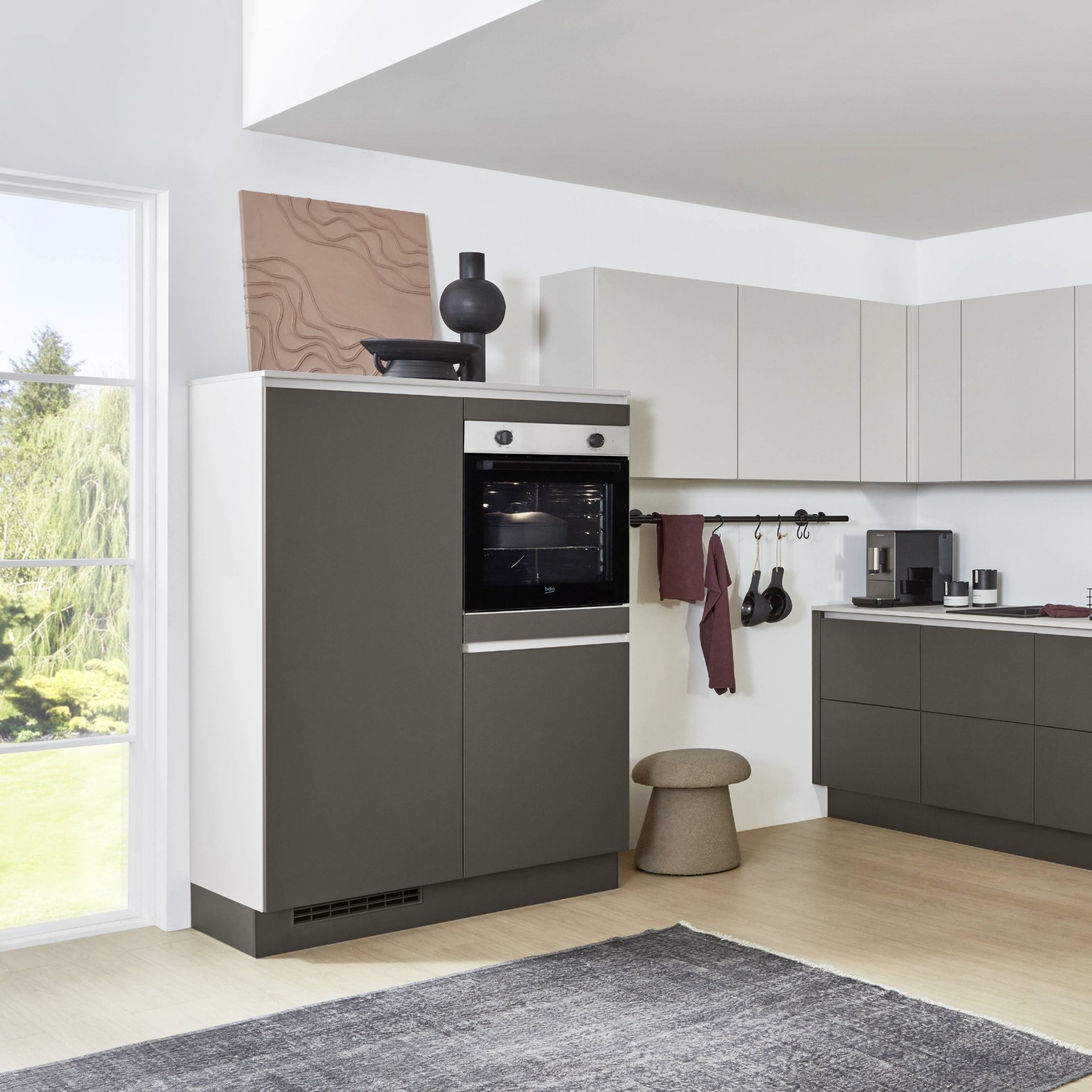 Dunkelgraues griffloses Highboard mit Einbaubackofen am Ende einer L-Küche, darüber helle Wandschränke, Nobilia Line N Look